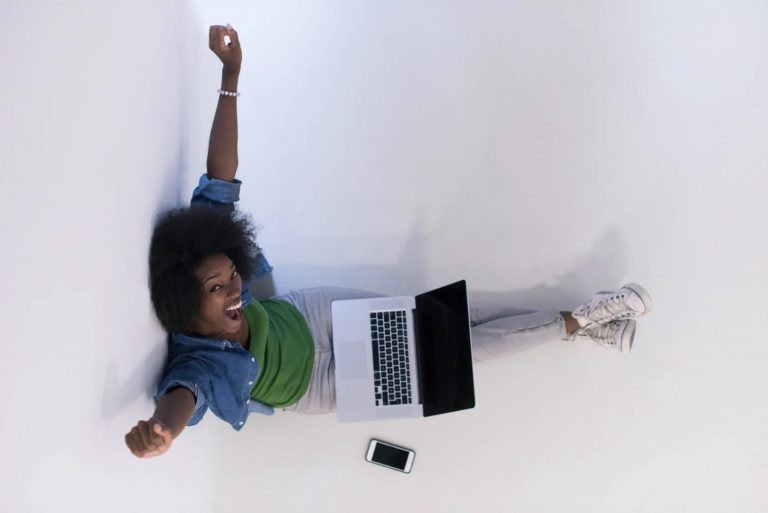 Une femme heureuse avec une ordinateur sur les jambes lève les bras